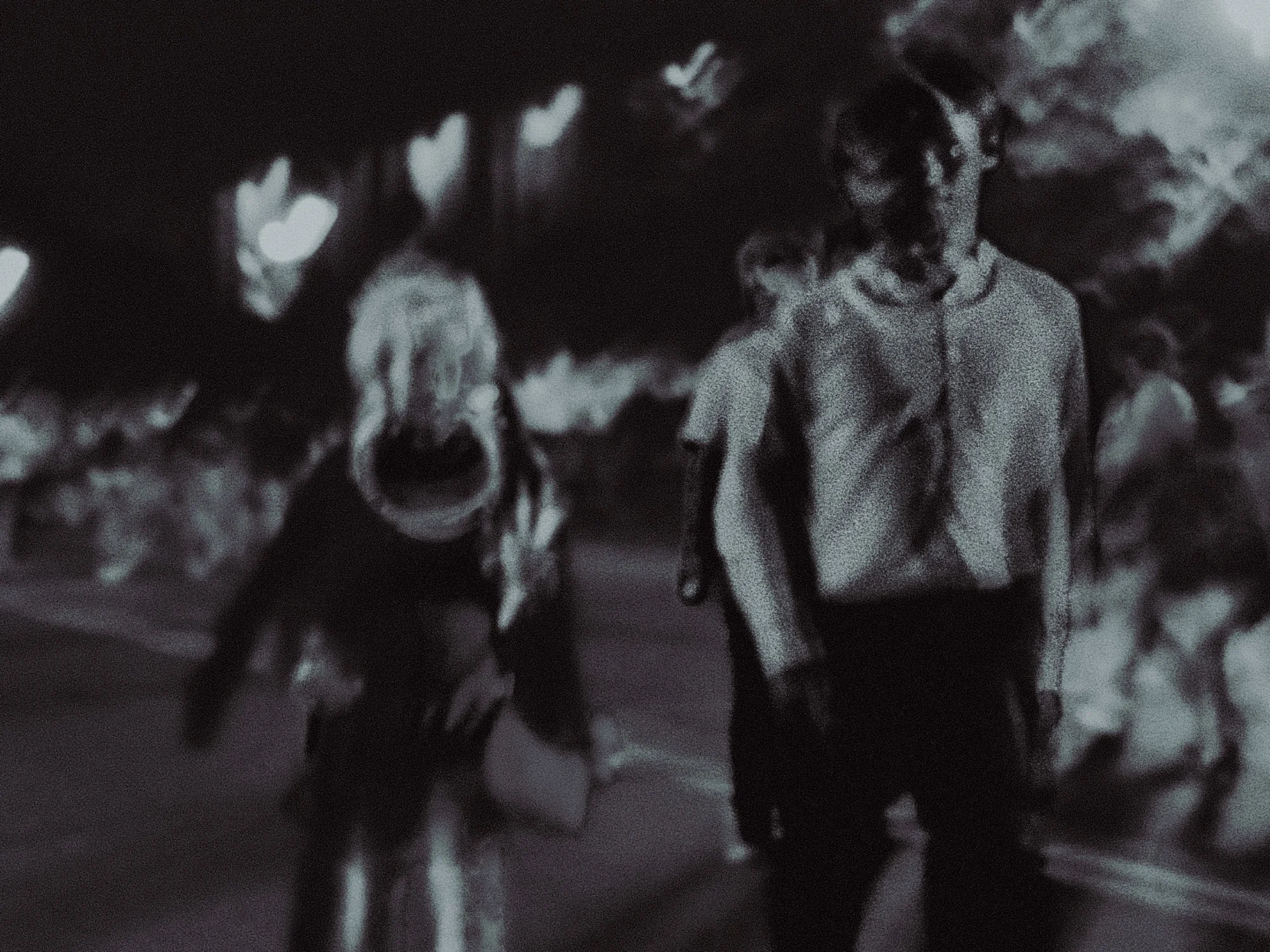 Two figures drifting through a night crowd, bokeh lights overhead